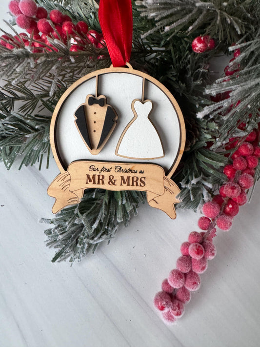 A wooden ornament with a bride and groom silhouette, surrounded by a wreath of red berries and greenery.