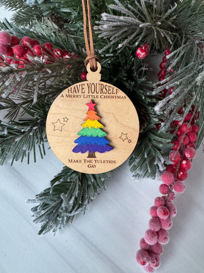 A wooden ornament with a colorful tree design hangs on a Christmas tree branch, surrounded by pine branches and red berries.