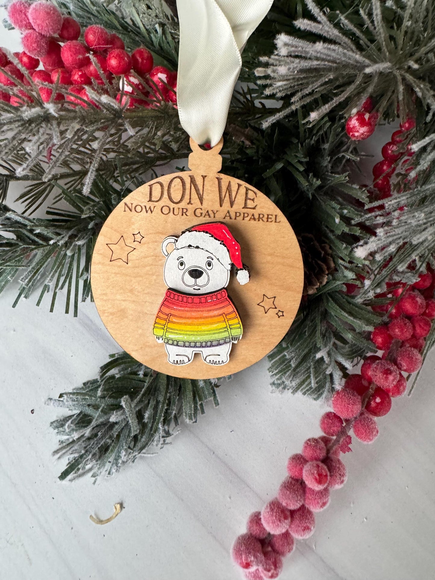 A wooden ornament with a polar bear wearing a colorful scarf, surrounded by a wreath of berries and pine branches.