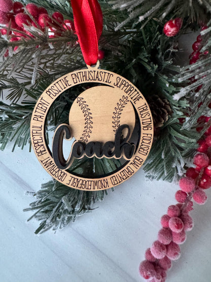 A wooden ornament with a baseball and the word "Loves" on it, placed on a pine branch with red berries.